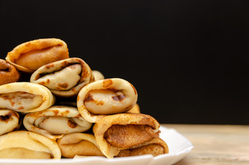 Many homemade thin pancakes with filling stacked pyramid on a white plate against a black wall, copy space