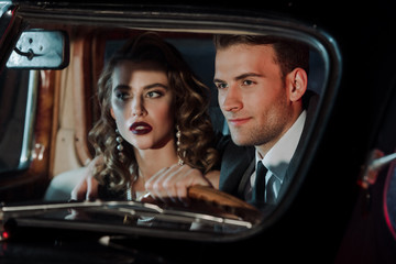 selective focus of happy man touching steering wheel and sitting near attractive woman in retro car