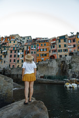 Fototapeta na wymiar Back view portrait of a blonde woman looking at the beautiful colorful buildings in Chinque Terre, Italy. Cinque Terre old seaside villages on the rugged Italian Riviera coastline