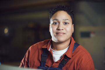 Head and shoulders portrait of female factory worker wearing overalls looking at camera and smiling...