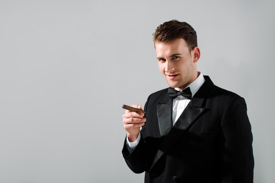 handsome man in suit holding cigar isolated on grey
