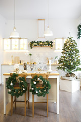Christmas decor. Bright interior of white kitchen with decorated Christmas tree, garlands and Christmas wreaths.