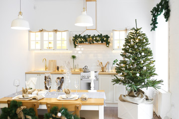 Christmas decor. Bright interior of white kitchen with decorated Christmas tree, garlands and Christmas wreaths.