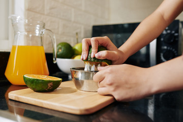 Close-up image of woman using manual metal squeezer when making fresh orange juice for breakfast