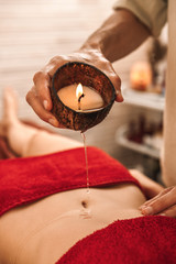 Alternative Medicine. Therapist healing lying woman doing massage with aroma candle pouring hot wax on belly close-up