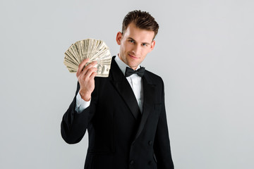 happy and rich man in suit holding dollar banknotes isolated on grey