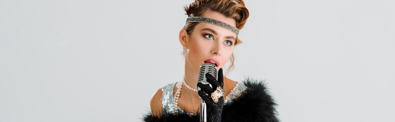 panoramic shot of attractive woman singing and touching retro microphone isolated on grey