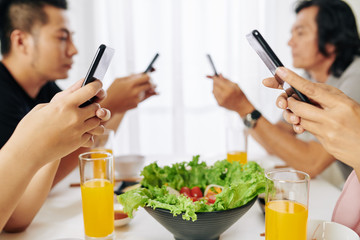 Family members texting and checking social media on smartphones instead of talking at breakfast