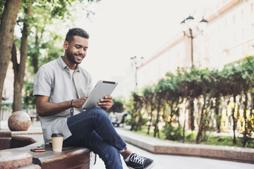 Smiling man student using digital tablet in a city. Young handsome men having coffee break. Modern lifestyle, connection, business, freelance work concept