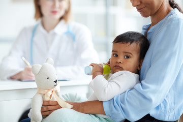 Portrait of baby boy lying on mother's knees and looking at camera while they visiting doctor at hospital