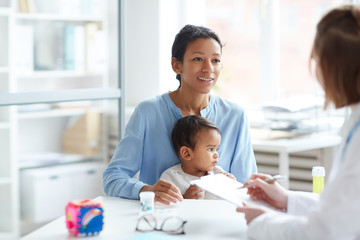 Young mother together with her baby sitting and talking to the pediatrician at doctor's office