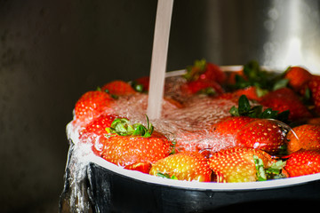 Water splashing on red strawberries in a bowl, rinsing ripe berries in a kitchen sink.