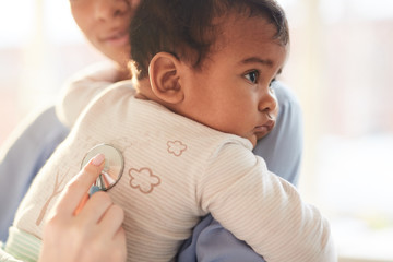 Close-up of mother holding baby on her hands with doctor listening to his heartbeat with stethoscope