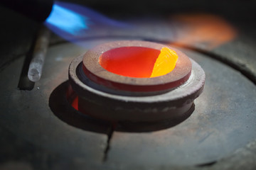 closeup picture of gold bar melting in liquid metal in furnace, glowing red-hot