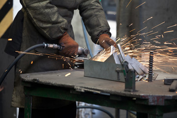 worker processing metal, lots of sparks, against factory industrial interior background