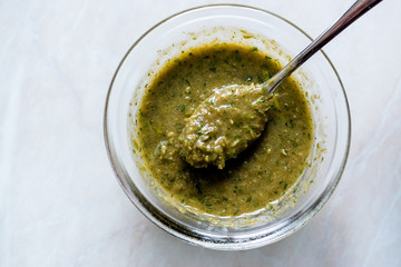 Homemade Green Herbal Salad Sauce with Plant Roots in Glass Bowl with Spoon.