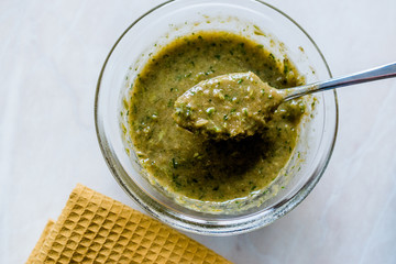 Homemade Green Herbal Salad Sauce with Plant Roots in Glass Bowl with Spoon.