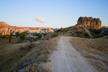 Dirt road in desert mountain landscape in Cappadocia. Sandstone hill illuminated with sunset light. Cappadocia, Anatolia, Turkey.