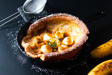 Food concept Homemade Dutch baby banana caramel topping pancake in skillet iron cast on black background