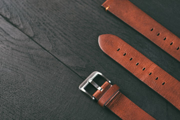 Light brown handmade leather straps with steel buckle laying on the dark wooden table. 