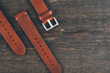 Handmade brown leather watch straps with steel buckle laying on the wooden table.