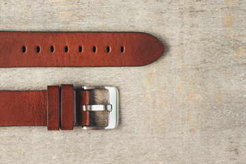 Brown leather handmade strap with steel buckle laying on the light brown wooden surface. Copy space for the text. 