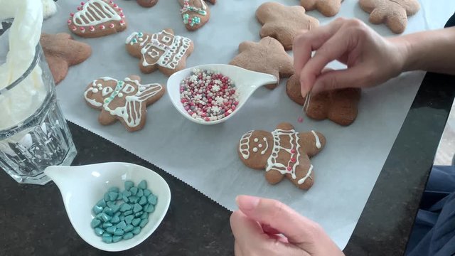 Making gingerbread cookies for christmas and holidays. Woman's hand putting pearls onto cookie to decorate it.