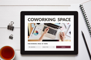 Coworking space concept on tablet screen with office objects on white wooden table. Top view
