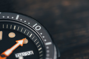 Close up of black diver watch dial. Rustic wooden background. Bezel with marks. Copy space. Top...