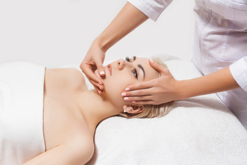 Obraz na płótnie Canvas Concept of therapeutic anti-aging skin tightening facial treatments. Close-up hands of an unidentified young woman masseur doing facial massage to beautiful young caucasian client woman at spa salon.