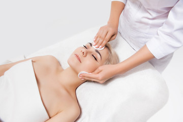 Obraz na płótnie Canvas Doctor beautician cleanses face skin with sponge in beauty salon. Perfect cleaning healthcare spa treatment. Skincare beauty spa concept. Model lying on couch with closed eyes in cosmetological clinic