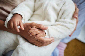 Close-up of mother holding her child's hands while holding him on hands and cradling him
