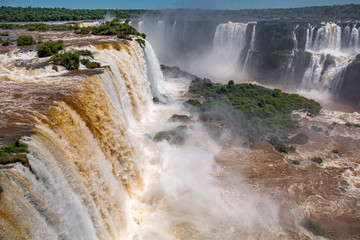 View of powerful Iguazu Falls near Devil´s Throat with brown and white water in lush green vegetation