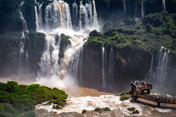 Close up view to spectacular waterfalls with lush green vegetation and a visitor platform, Iguazu Falls, Argentina