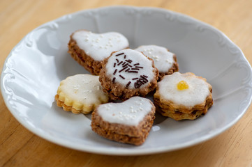Jam and cream filled cookies with sugar sweet white icing on white plate on wooden table, group of Christmas sweets