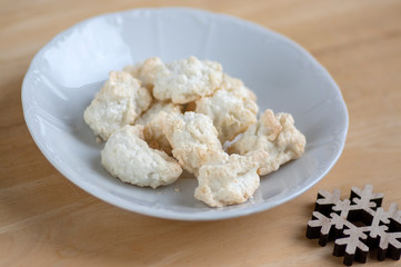 Coconuts made of egg whites, sugar and shredded coconut on white plate on wooden table, group of Christmas sweets