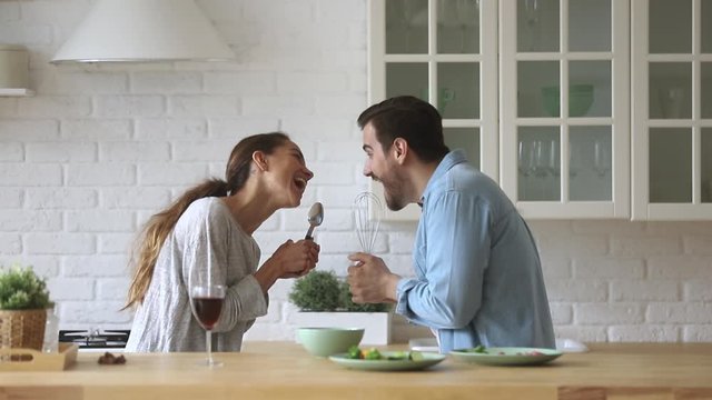 Young happy couple singing preparing healthy food cooking in kitchen