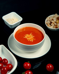 a plate of tomato soup with grated cheese and crackers