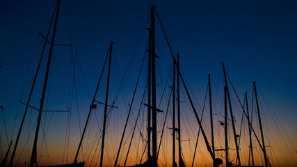 Sunset by the sea. Masts of boats in the harbor. The glare of the sun at the sea.