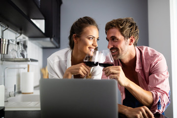 Young couple relaxing in kitchen with wine and laptop. Love, technology, people concept.