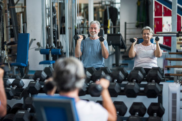mature man with his wife doing exercise of biceps at the gym - fitness and healthy lifestyle...