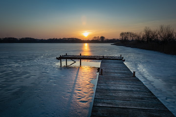 Obraz premium Wooden bridge made of boards, frozen lake and sunset