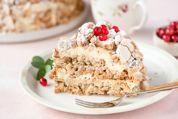 Hazelnut Daquoise cake or Kiev cake with meringue layers and vanilla buttercream served on white plate, pink background