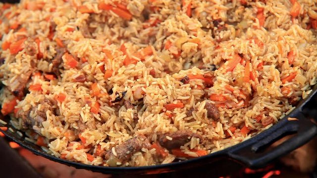 Authentic Uzbek pilaf (plov) waiting to be served in pan over open fire. Foodie background, food preparation concept.