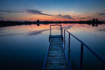 Fototapeta na wymiar Jetty on a calm lake and sunset, evening beauty view
