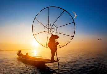 Burmese fisherman on bamboo boat catching fish in traditional way with handmade net. Inle lake,...