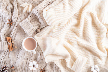 Autumn or winter composition. Coffee cup, cinnamon sticks, anise stars, beige sweater on cream color knitted blanket background. Flat lay top view copy space.