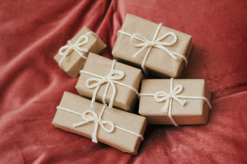 Presents for a Christmas. Gift boxes wrapped in craft paper and tie white string. Red velvet cloth background. Holiday mood.	