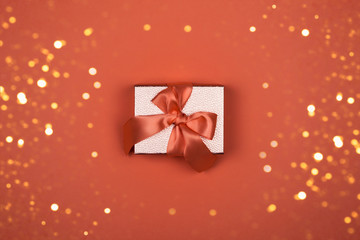 Gift box on orange background with shining sparkles. Satin ribbon bow, box bronze color. Luxury gift, place for text. Holidays and birthday concept, christmas festive decor. Layout for design.