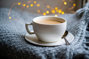 Cup of coffee with milk on cozy knitted winter blanket